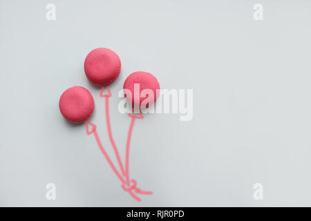 Three pink macaroons in the form of balloons on a blue background. Stock Photo