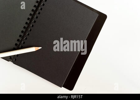 Black paper spiral notebook and white pencil Stock Photo
