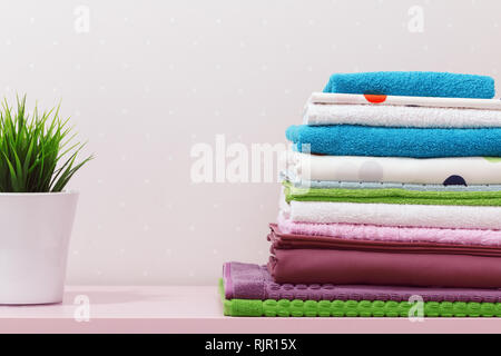 On the dresser there is a stack of clean ironed bed linen, folded multi-colored towels and a home plant stands. Stock Photo