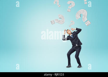 Grey question marks falling on a businessman on blue background. Questions and answers. Business solutions. Management and planning. Stock Photo