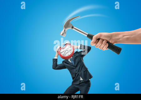 Man's hand holding a hammer and hitting a miniatured businessman on the alarm clock which he has instead of his head. Miss deadline. Business problems Stock Photo