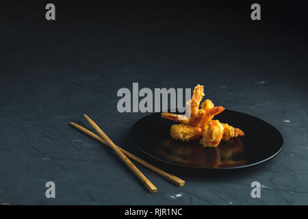 Fried Shrimps tempura in black plate on dark concrete surface background. Copy space for you text. Seafood tempura dish of traditional asian cuisine. Stock Photo