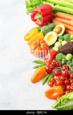 Fresh raw ingredients for salad, tomatoes cucumbers lettuce pepper avocado celery spring onion broccoli peas on the white table, copy space Stock Photo