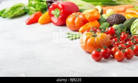 Fresh raw ingredients for salad, tomatoes cucumbers lettuce pepper avocado celery spring onion broccoli peas on the white table, copy space Stock Photo