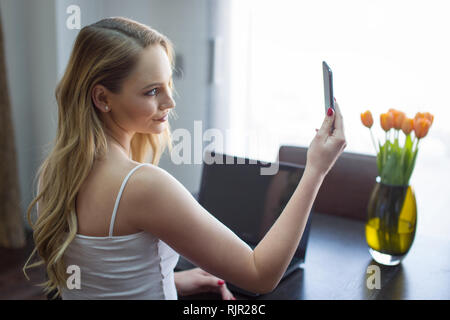 Young blonde woman video calling on smartphone at home Stock Photo
