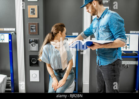 Young woman with salesman or repairmman choosing a new ceramic bowl with drain system in the plumbing shop Stock Photo