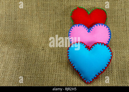 Valentine Day template, handmade red, pink and blue foam sheet stitched toy hearts on jute canvas, close up, high angle view. Love, relationship, Vale Stock Photo