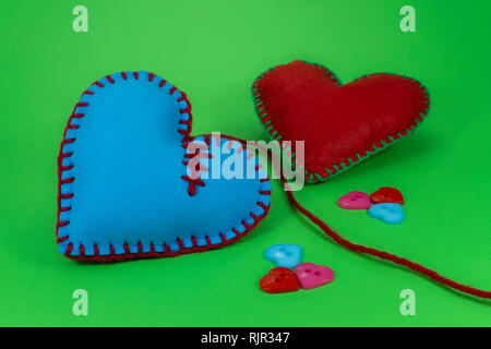 Heart shaped hand stitched textile hearts made of pink fabric and sewed with blue threads on green chromakey background for romantic or Valentines con Stock Photo
