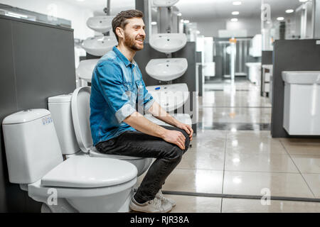 Man choosing lavatory pan sitting on it in the building shop with sanitary ceramics Stock Photo