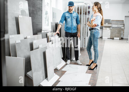 Young woman customer choosing tiles standing with seller or repairman in the ceramic shop Stock Photo