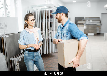 Young woman customer standing with worker or delivery man carrying packaging with purchase in the ceramic shop Stock Photo