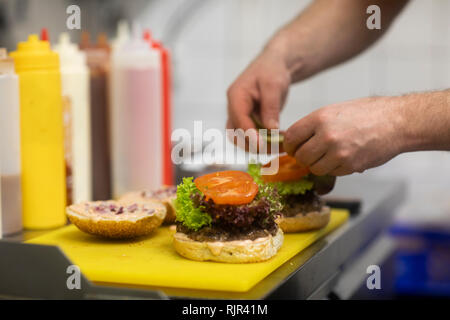 Fast food worker adding salad to hamburger in commercial kitchen, close up of hand Stock Photo