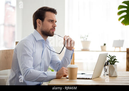 Thoughtful serious businessman lost in thoughts at work with laptop Stock Photo