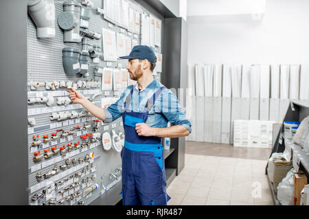 Handsome workman choosing water pipes and pipe joints standing near the showcase in the plumbing shop Stock Photo