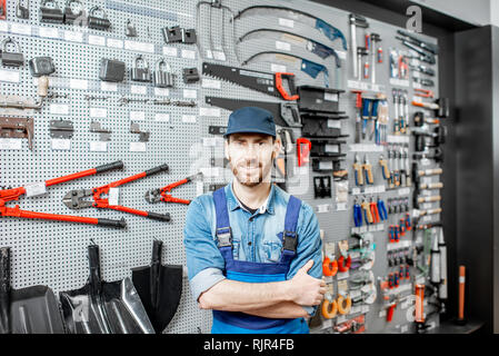 Portrait of a handsome worker in uniform standing in the shop with garden equipment on the background Stock Photo