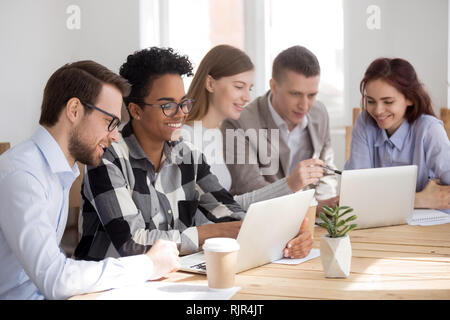 Happy diverse research team working on laptops cooperating brainstorming Stock Photo