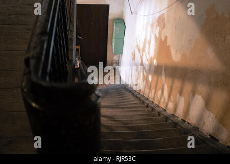 empty worn wooden staircase leading down to a door with shadows on the wall Stock Photo