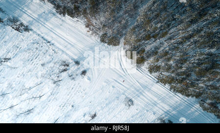 Aerial view of road passing through the snow-covered winter forest. Top view