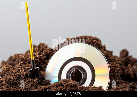 The CD is half buried in the ground, next to a shovel Stock Photo