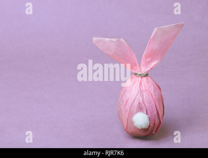 Easter egg in the form of a cute pink Easter bunny on a gentle purple background Stock Photo