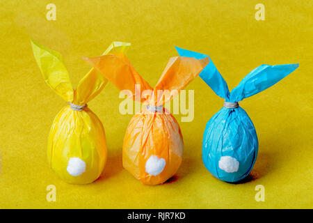 Three colorful Easter eggs in the form of Easter rabbits on a bright yellow background Stock Photo