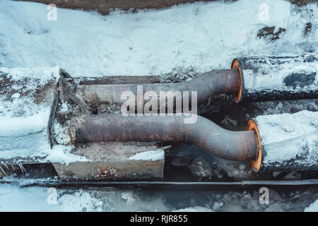 Two welded steel pipes with insulation in a snowy trench with some water in the bottom Stock Photo