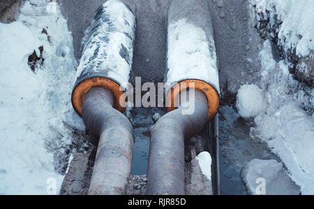 Two welded steel pipes with insulation in a snowy trench with some water in the bottom Stock Photo