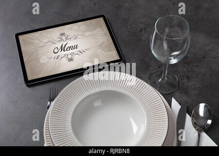 Tablet with stylish restaurant logo and laid table  Stock Photo