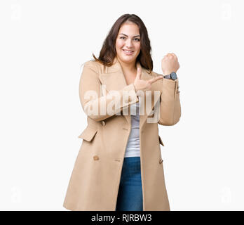 Beautiful plus size young woman wearing winter coat over isolated background In hurry pointing to watch time, impatience, upset and angry for deadline Stock Photo