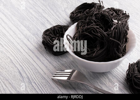 Black pasta in a white plate on a white table against a shiny background with a fork. The concept of unusual rare dishes. Made from durum wheat with c Stock Photo