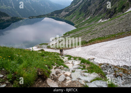 A hiker climbs up the side of Mt. Rysy near Czarny Staw pod Rysami (Black Lake) near an ice field in the Tatra National Park,Lesser Poland Vovoidship, Stock Photo