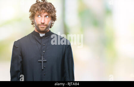 Handsome hispanic catholic priest man over isolated background smiling looking side and staring away thinking. Stock Photo