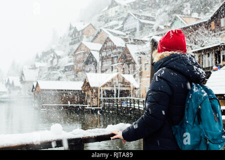 Woman in red hat enjoying the view over lakefront Hallstatt old town during snow storm, Austria. Stock Photo
