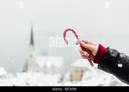 Woman holding red candycane with snowy Hallstatt old town on background, Austria Stock Photo