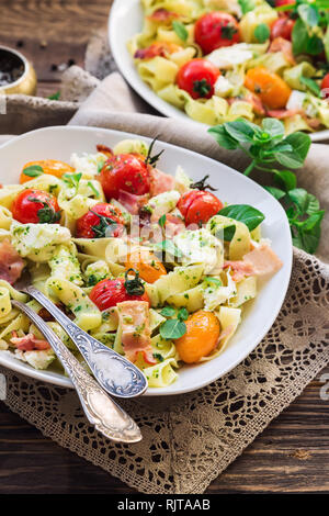Fettuccine pasta with baked tomatoes, bacon and mozzarella cheese on rustic wooden background. Stock Photo