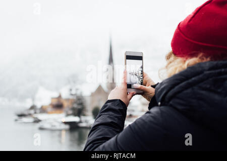 Woman in red hat taking picture of Hallstatt old town during snow storm, Austria.
