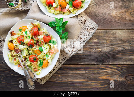 Fettuccine pasta with baked tomatoes, bacon and mozzarella cheese on rustic wooden background. Top view. Stock Photo