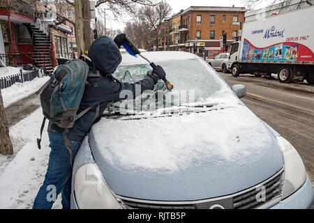 Montreal, Canada - 7 February 2019: man cleaning car windshield from ice with scraper tool. Stock Photo