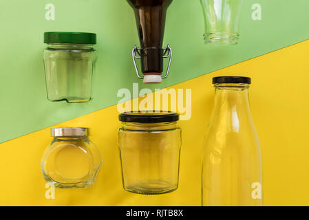 Empty glass jar and bottle on yellow and green background, view from the top Stock Photo
