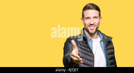 Handsome man wearing winter coat smiling friendly offering handshake as greeting and welcoming. Successful business. Stock Photo