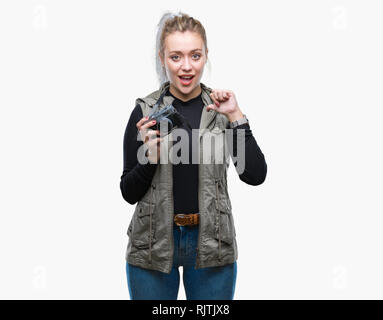 Young blonde woman taking pictures using vintage camera over isolated background with surprise face pointing finger to himself Stock Photo