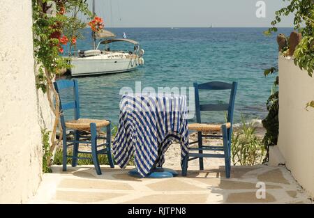 Traditional Greek blue table and chairs by the Aegean sea, Aegina island Stock Photo