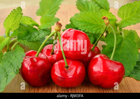 Bunch of  cherries with stems and lemon balm leaves on dark wooden surface Stock Photo