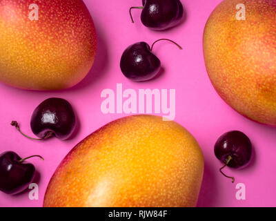 Three Mangos Five Black Cherries on Bright Pink Background Stock Photo