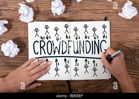 An Overhead View Of A Businesswoman's Hand Drawing Crowdfunding Concept On Wooden Textured Desk Stock Photo