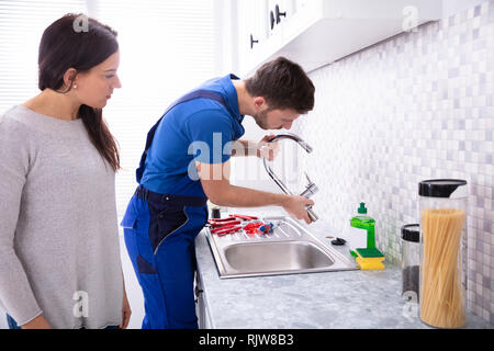 Young Woman Looking At Male Plumber Fixing Faucet In Kitchen Stock Photo