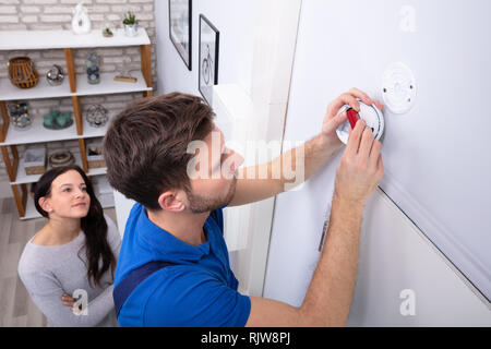 Happy Woman Standing Near Serviceman Replacing Battery In Smoke Alarm Stock Photo