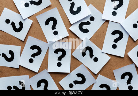 question marks on paper cards scattered randomly over a wooden background in a conceptual image Stock Photo