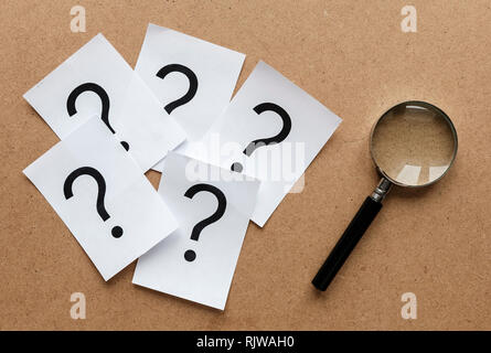 Question marks printed on white cards lying on a wooden background with a magnifying glass in a conceptual image Stock Photo