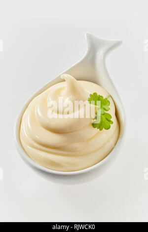 Twirled freshly made mayonnaise in a ceramic spoon to be served as an accompaniment to a formal meal high angle on white Stock Photo